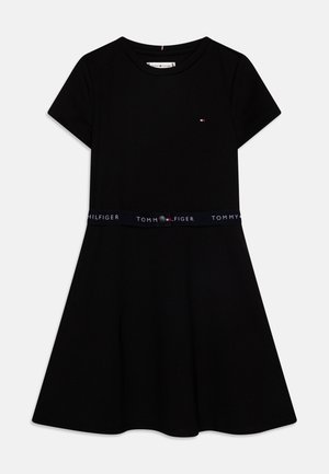 Vestido negro de manga corta con falda acampanada. Presenta un logotipo en el pecho y una cinturilla elástica azul marino con el texto "TOMMY HILFIGER".