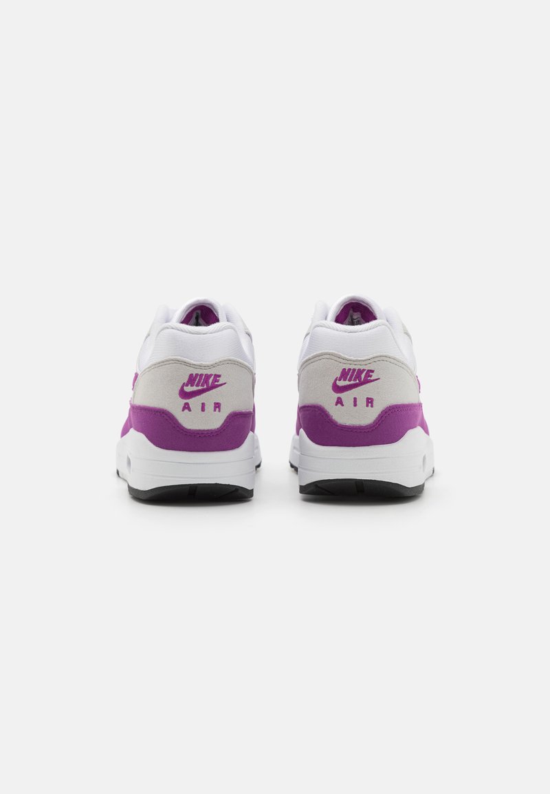 Nike Air sneakers met een bovenwerk van witte mesh, lichte grijze suede accenten en een paarse hielpanal met branding; zwarte zool.