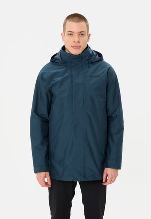 Veste imperméable marine avec capuche, présentant une coupe droite, une fermeture éclair et deux poches latérales. Texture lisse et minimalisme de la marque.