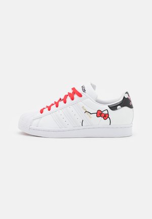 Witte leren sneakers met rode veters, met een Hello Kitty ontwerp aan de zijkant en een zwarte hieltab met stippen. Rubberen zool.