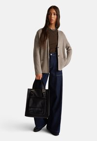 Béžový pletený kardigan s knoflíky, hnědý top, široké denimové kalhoty a černá taška přes rameno se stříbrným kováním a přední kapsou.