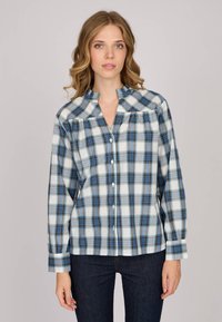 Chemise à manches longues en tartan blanc, bleu et noir. Dotée d'un col mandarin et d'une fermeture à boutons sur le devant avec un tissu doux et texturé.