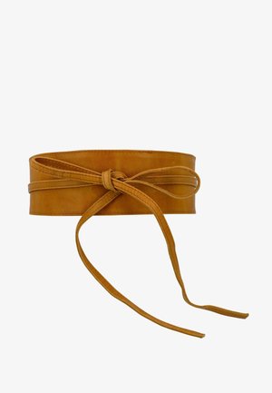Large ceinture en cuir beige avec un nœud en forme de papillon noué à l'avant, avec de longues extrémités lâches sur fond blanc.