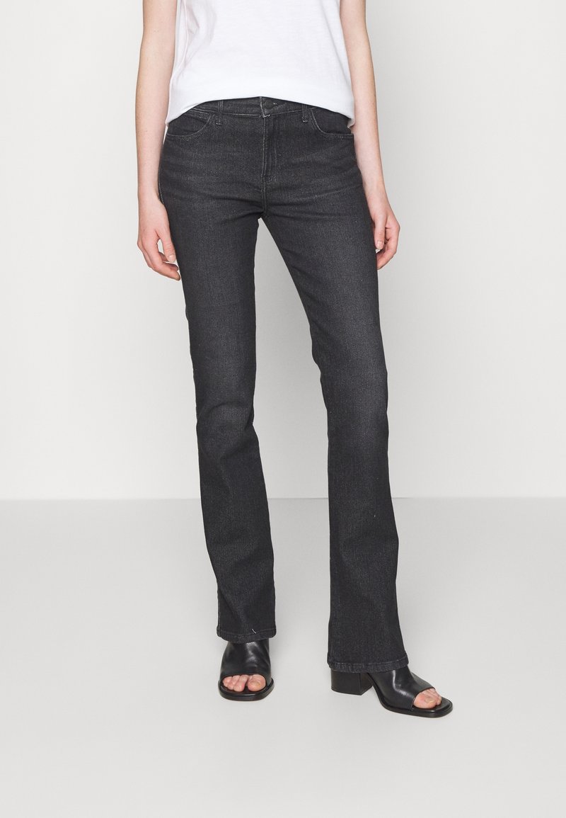 Svarta utsvängda jeans i denim, med fem fickor, knappknäppning och subtila sömmar. Matchat med en enkel vit topp och svarta sandaler.