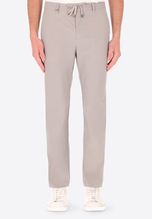 Pantaloni beige a gamba dritta con vita con bottone e coulisse, indossati con scarpe da ginnastica bianche su una persona in piedi.
