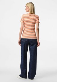 Svītrains oranžs un balts ribots T-krekls saskaņots ar tumši ziliem platām kājām džinsiem. Krekls ir ar īsām piedurknēm un pieguļošu siluetu.