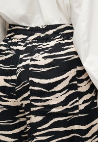 Μαύρο και μπεζ παντελόνι με ρίγες ζέβρας, ελαστική μέση και πίσω τσέπη με μαύρο κουμπί. Μαλακό ύφασμα και φαρδιά γραμμή.