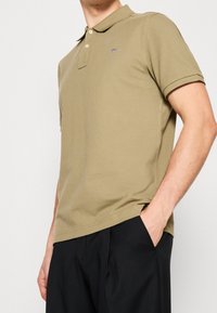 Khaki polo tričko vyrobené z bavlny, má límec a krátké rukávy. Malá emblematická nášivka na prsou, strukturovaná tkanina, rovný střih.
