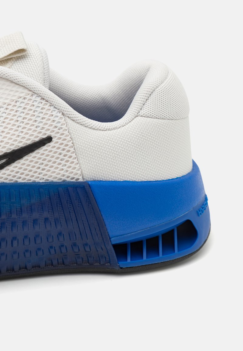 Witte sportschoen met bovenwerk van mesh, zwart logo en een blauwe rubberen hak. Beschikt over gestructureerde details en een ventilatie-uitsnijding op de zool.