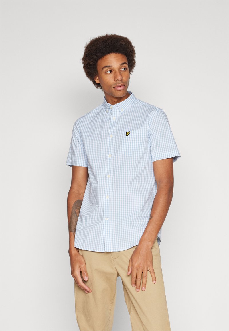 Blue and white checkered short-sleeve shirt with button-down collar and small yellow logo on the chest. Cotton fabric, regular fit.