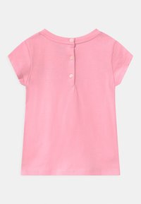 Camiseta de niño pequeño de color rosa con mangas cortas y tres botones en la parte posterior del cuello, hecha de suave algodón.