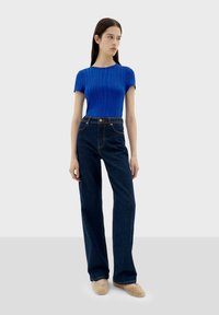 Haut bleu côtelé à manches courtes associé à un jean bleu foncé taille haute, avec une jambe droite, des coutures discrètes et des chaussures de couleur claire.
