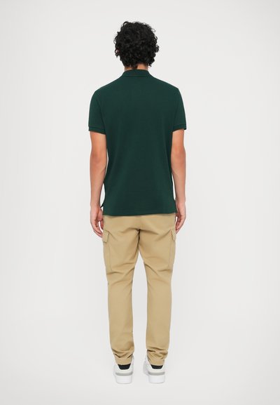 Mörkgrön polo t-shirt med krage, tillsammans med beige cargobyxor och vita sneakers. Synlig sömnad och cargofickor på byxorna.