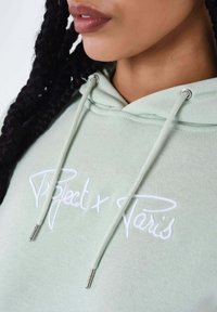 Felpa verde chiaro realizzata in morbido tessuto, con logo ricamato bianco "Project x Paris" e accessori in metallo argentato sui lacci.
