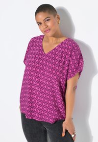 Top a V collo, morbido e di un vivace colore rosa con un motivo a rombi. Maniche corte e tessuto leggero, abbinato a jeans grigio scuro.