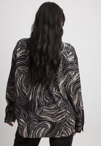 Blusa nera con motivo astratto a spirale crema, maniche lunghe, vestibilità ampia, texture morbida e polsini con bottoni.
