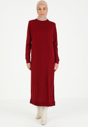 Long red dress with ribbed texture and subtle patterns, featuring long sleeves and a crew neck. Worn with cream knee-high boots.
