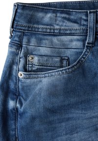 Jeans de mezclilla en un lavado azul medio, con una cintura estándar, bolsillo frontal con herrajes de plata y detalles de costura visibles.