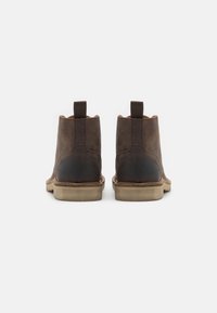 Botas de tobillo de cuero marrón con un acabado suave, paneles laterales elásticos y un tacón trasero elevado. Presentan una suela de goma de color claro.