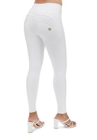 Leggings blancs au toucher lisse, avec des poches arrière et un petit accent de marque. Associés à des sandales blanches à talons carrés.