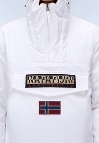 Biała nylonowa kurtka z wysokim kołnierzem, przednia kieszeń z czarną i beżową naszywką z logo oraz czerwoną naszywką z norweską flagą.