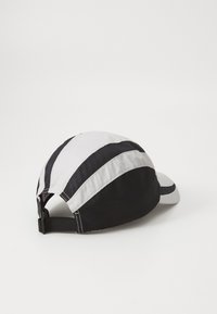 Baseball caps med svart og hvit alternerende striper, buet skygge, justerbar stropp bak, laget av teksturert materiale.