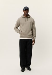 Μπεζ φούτερ με κορδόνι και μπροστινή τσέπη, συνδυασμένο με μαύρο φαρδύ παντελόνι με σχέδιο και μαύρα παπούτσια. Καθημερινή εμφάνιση.