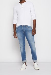 Bílá dlouhá halenka s knoflíky, doplněná o světle modré slim-fit džíny a bílé tenisky s šedými detaily.