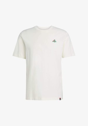 T-shirt en coton couleur crème avec des manches courtes, un col rond et un petit graphisme vert et rouge sur la poitrine gauche. Étiquette avec le logo visible sur le côté.