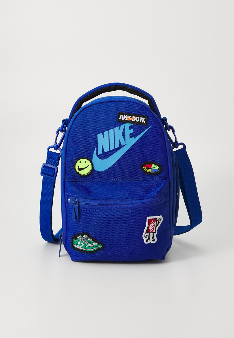 Blue Nike backpack with zippered front pocket and adjustable strap, featuring embroidered patches, including a smiley face and shoes.