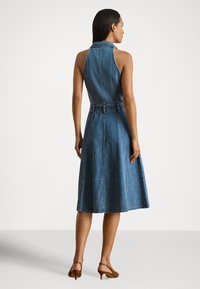 Džinsa kleita ar augstu apkakli, bez piedurknēm un A līnijas siluetu. Aprīkota ar jostu pie vidukļa un vidēja garuma apakšmalu. Krāsa: zila.