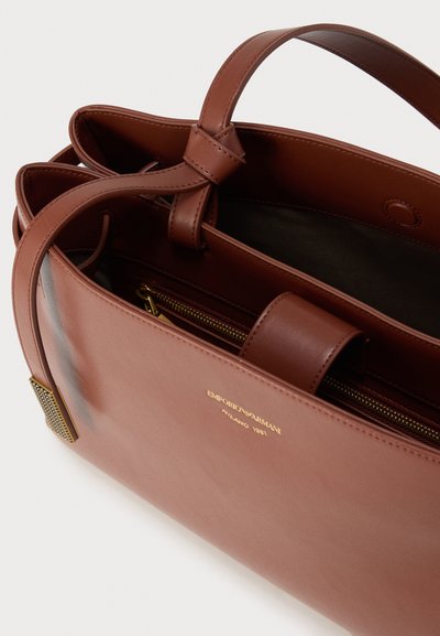 Καφέ δερμάτινη γυναικεία τσάντα με λεία υφή, διαθέτει φερμουάρ σε μία τσέπη, διπλές λαβές και χρυσό λογότυπο στο εμπρόσθιο μέρος.