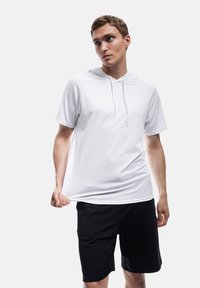 Weißes Kurzarm-Hoodie mit Kordelzügen, kombiniert mit schwarzen Shorts. Der Stoff wirkt glatt mit einer lockeren Passform.