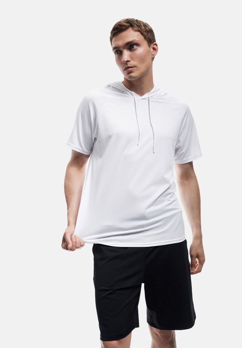 Weißes Kurzarm-Hoodie mit Kordelzügen, kombiniert mit schwarzen Shorts. Der Stoff wirkt glatt mit einer lockeren Passform.