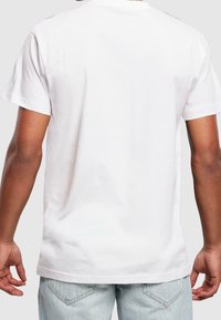 Bílá bavlněná tričko s kulatým výstřihem a krátkými rukávy, s hladkou texturou a volným střihem, zobrazené ze zadní strany.