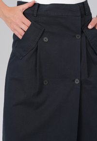 Jupe noire taille haute avec des boutons doublés et de grandes poches. Fabriquée en tissu lisse avec une coupe ajustée.