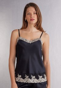 Svart satin camisole med v-ringning och beige spetskant vid axlarna och nederkant. Justerbara svarta band. Intrikat spetsmönster.