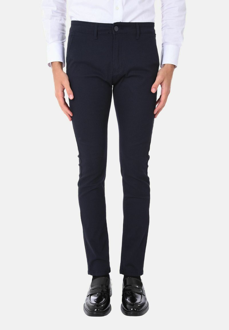 Pantaloni fitted blu navy in un materiale testurizzato, con chiusura a bottone e tasche frontali, abbinati a mocassini neri lucidi.