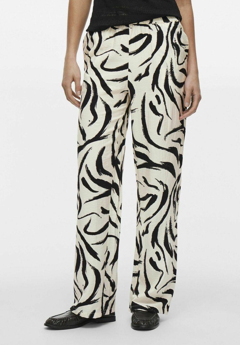 Pantalons larges en tissu crème avec de bold motifs abstraits en noir en forme de tourbillon. Dotés d'une taille élastique. Portés avec des ballerines noires.