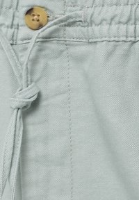 Tissu bleu clair avec une surface texturée, présentant un bouton rond couleur beige et un cordon ajustable noué le long de la ceinture.