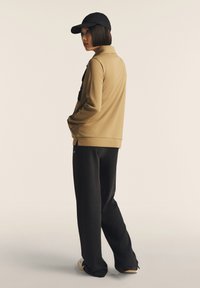 Sudadera beige con cuello alto, pantalones negros y una gorra negra, con un corte relajado y una textura suave. Diseño simple sin patrones.