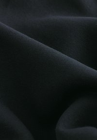 Zwarte stof met een gladde textuur en fijne weefsels, die natuurlijk valt in zachte plooien. Het materiaal lijkt lichtgewicht en flexibel.