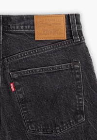El bolsillo trasero de unos jeans Levi's gris oscuro con la etiqueta roja distintiva y un parche de cuero marrón de la marca Levi Strauss & Co. encima de la cintura.
