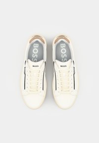 Baskets en cuir blanc avec des accents beiges, des rayures noires et des semelles intérieures grises. Dotées de lacets traditionnels et d'un design de talon arrondi.