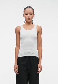 Biała bezrękawnikowa koszulka z miękkiego materiału, z okrągłym dekoltem i dopasowanym fasonem, zestawiona z luźnymi czarnymi spodniami.