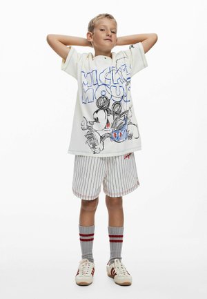 Valge t-särk sinise joonistusega Mickey Mousest, triibulised lühikesed püksid, hallid sokid punaste triipudega ja heledad spordijalatsid. Lastele mõeldud igapäevane riietus.