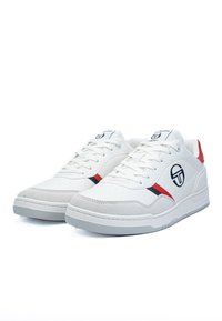 Scarpe sportive bianche con tomaia in pelle liscia, dettagli rossi e neri, punta bucherellata e logo sul lato e sulla linguetta.