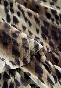 Brown and black patterned fabric with soft texture, featuring an abstract design of shapes and subtle sheen, folded in layers.