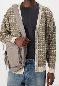 Stickad kofta i olivgrönt och creme med öppen framkant; grå axelväska; svart t-shirt; blå jeans; texturerat tyg med ribbade detaljer.