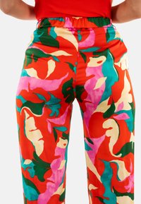 Pantaloni ampi e colorati di colore rosso con motivi astratti in rosa, verde e crema; tessuto morbido; cintura elasticizzata per il massimo comfort.